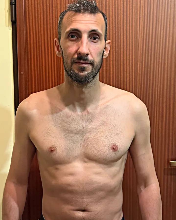 O fundador em casa, em tronco nu, de frente para a câmara, já com mais massa muscular.